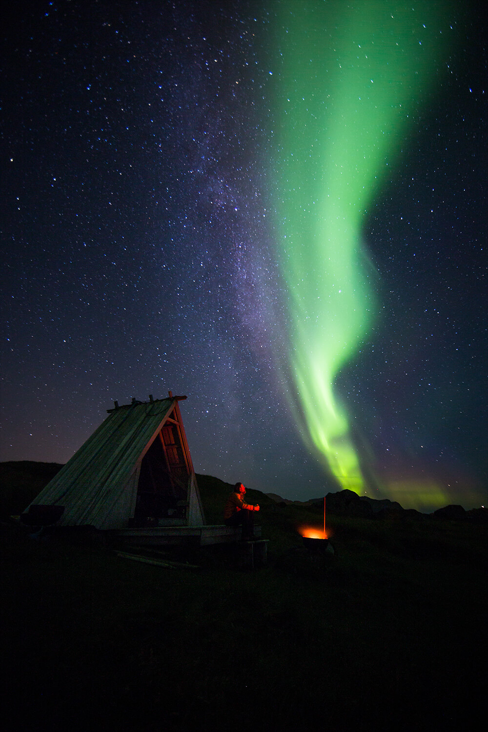 A person in front of a bonfire under the northern lights. Image by Neil Bloem