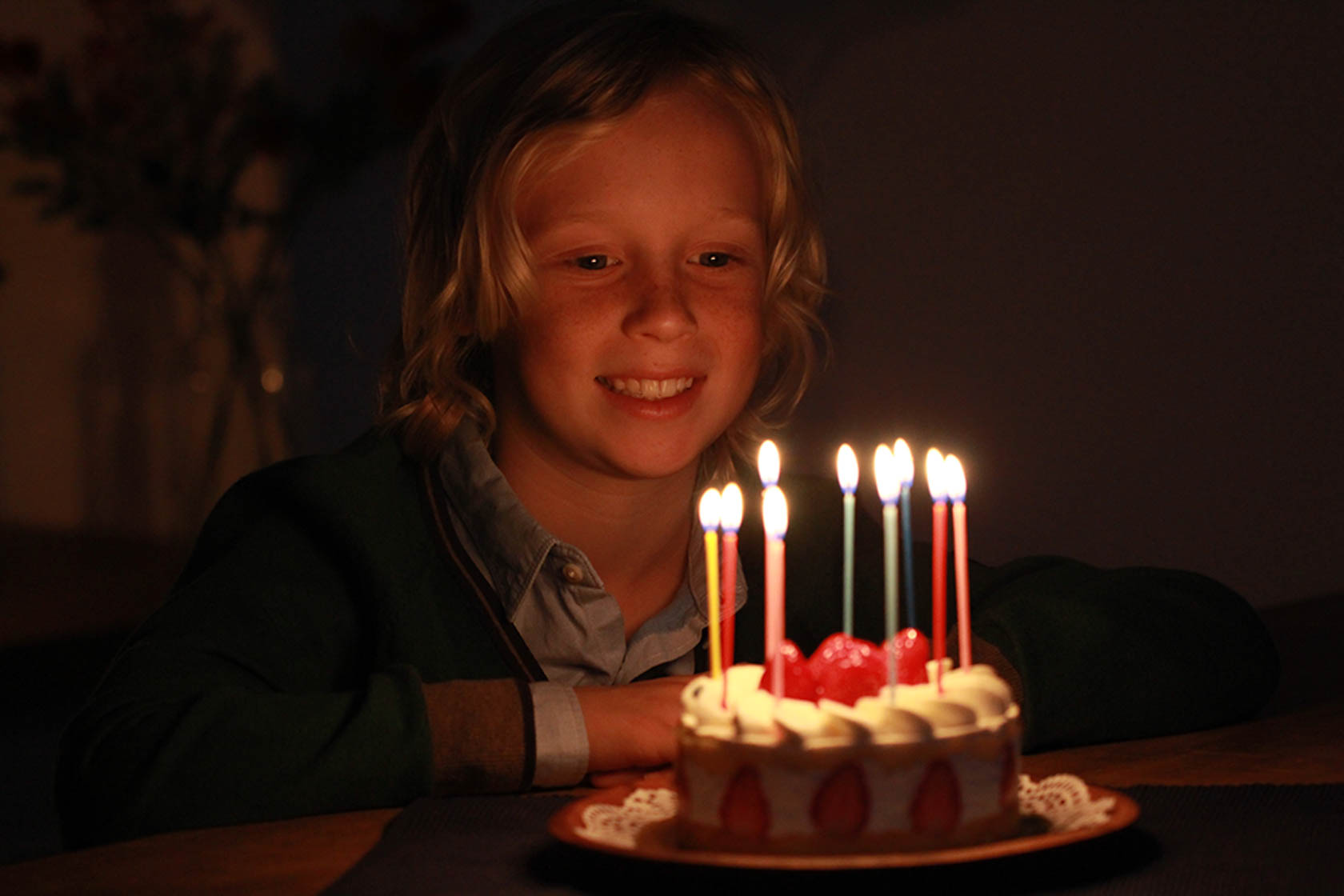 Young child sitting in front of a birthday cake with candles taken with Canon EOS 1300D DSLR camera