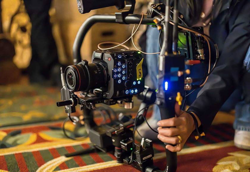 A canon cinema camera in a rig with lots of cables and accessories, being gently rested on the ground