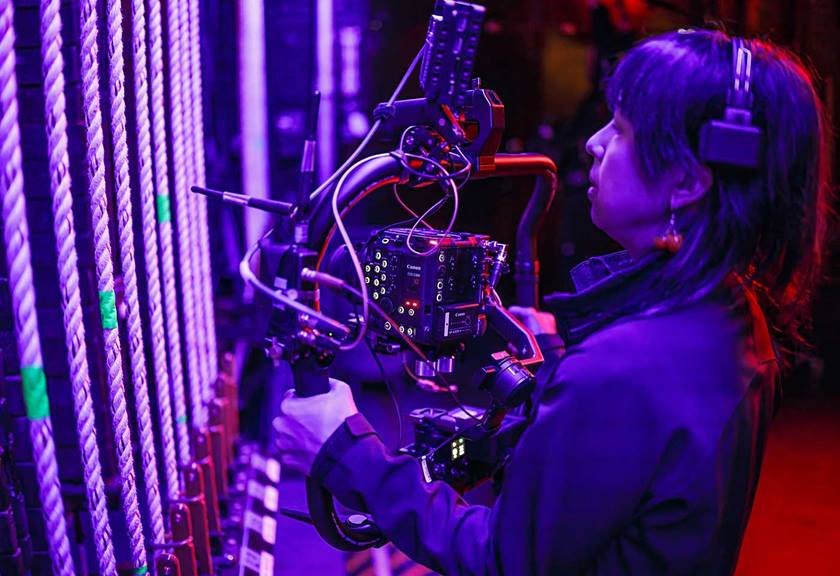 Woman with headset operating large camera rig in purple lighting