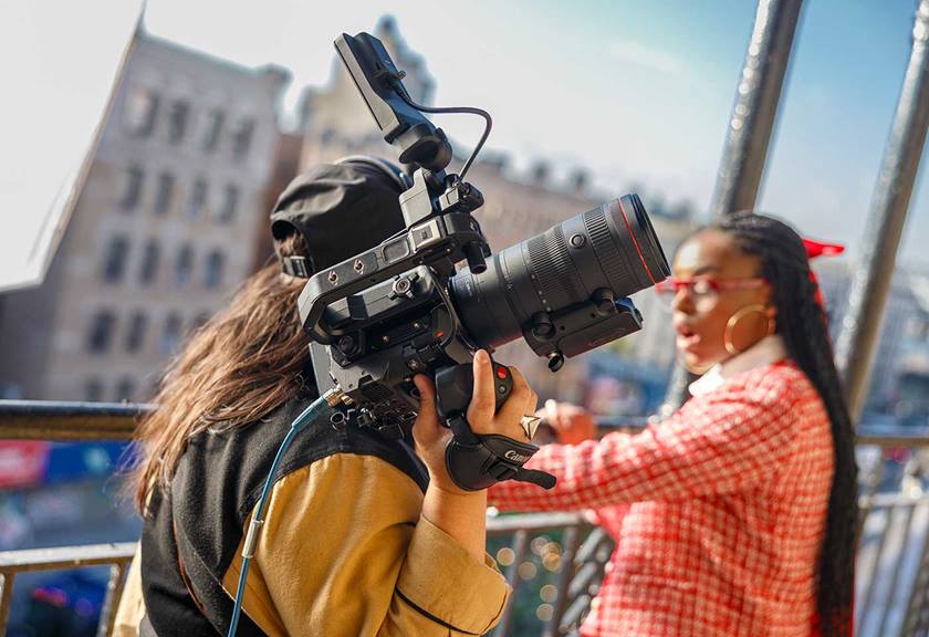 Women holding large camera with long lens on her shoulder, during a shoot on a balcony