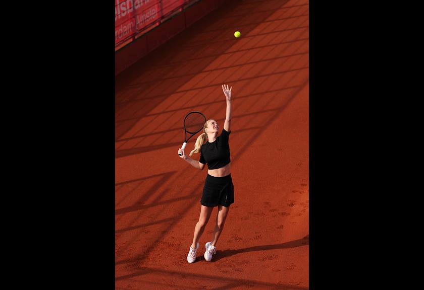 Image of a tennis player in black outfit about to hit the ball