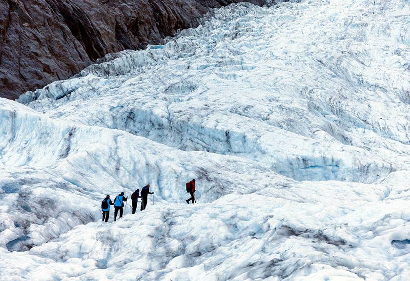 Trail of people hiking up rocky and icy formations