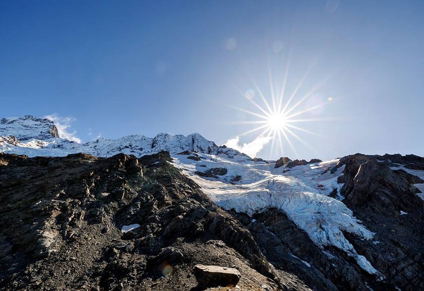 Sun shining behind icy glacier and mountain ranges