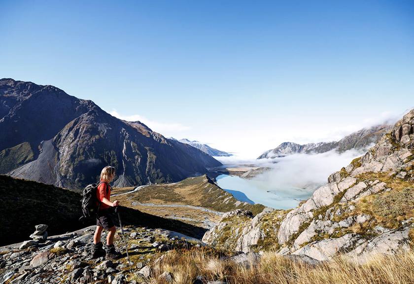 Person hiking up overseeing a view of mountains, clouds and lake