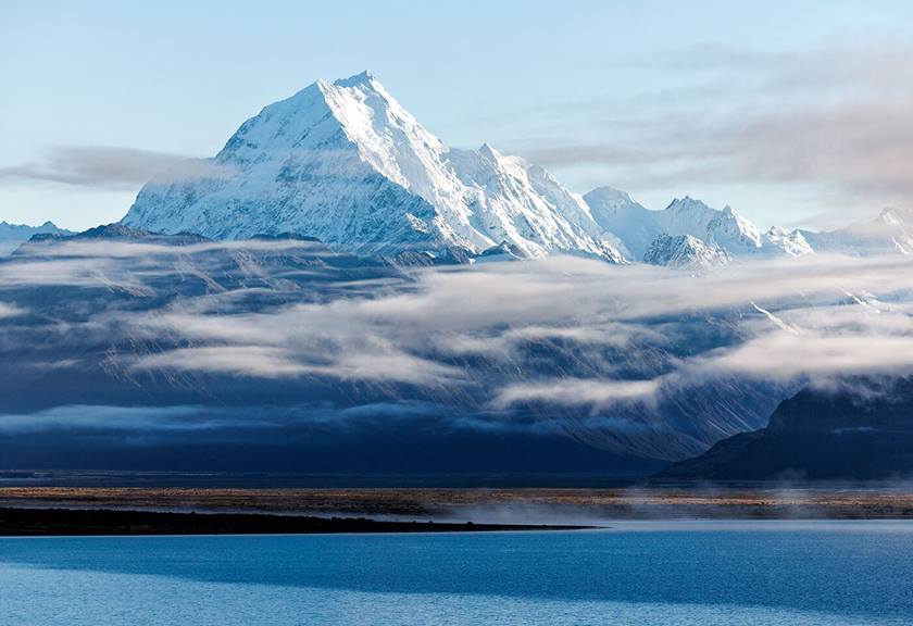 Snowy ice cap mountain ranges with clouds and lake in foreground