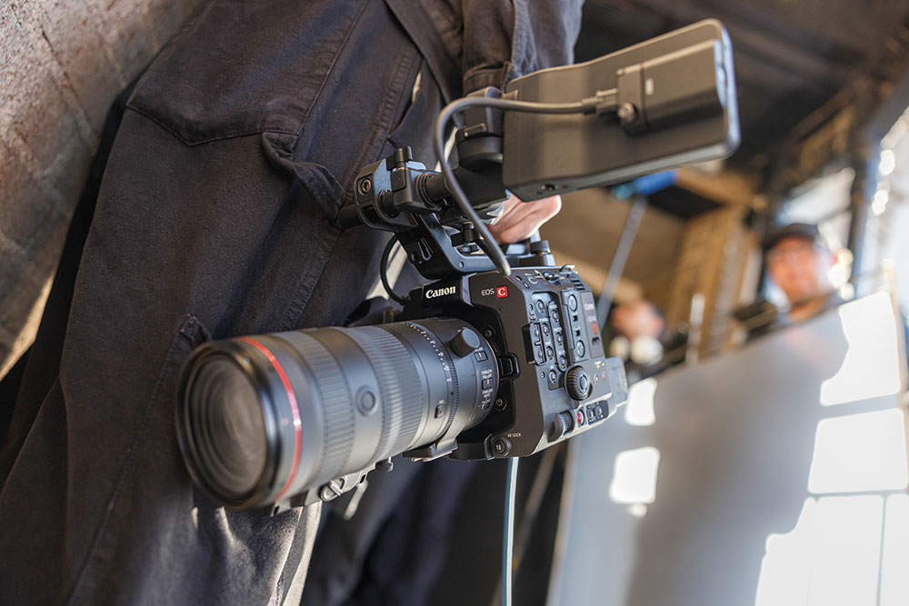 Someone holding cinema camera by their side with long lens attached to it