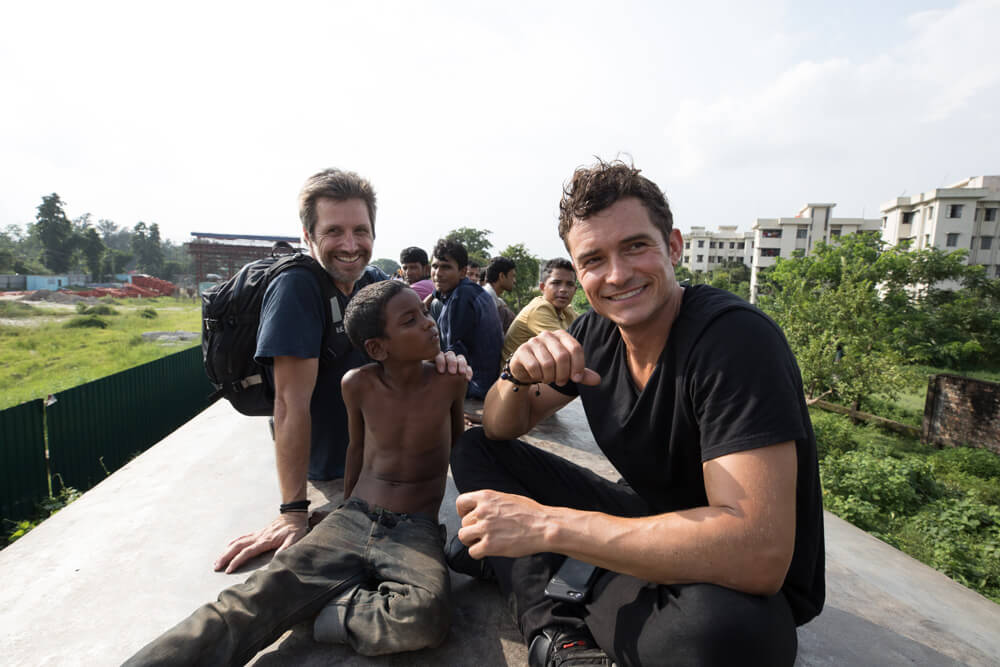 photo of Simon Lister and Orlando Bloom with children on top of a train in Bangladesh