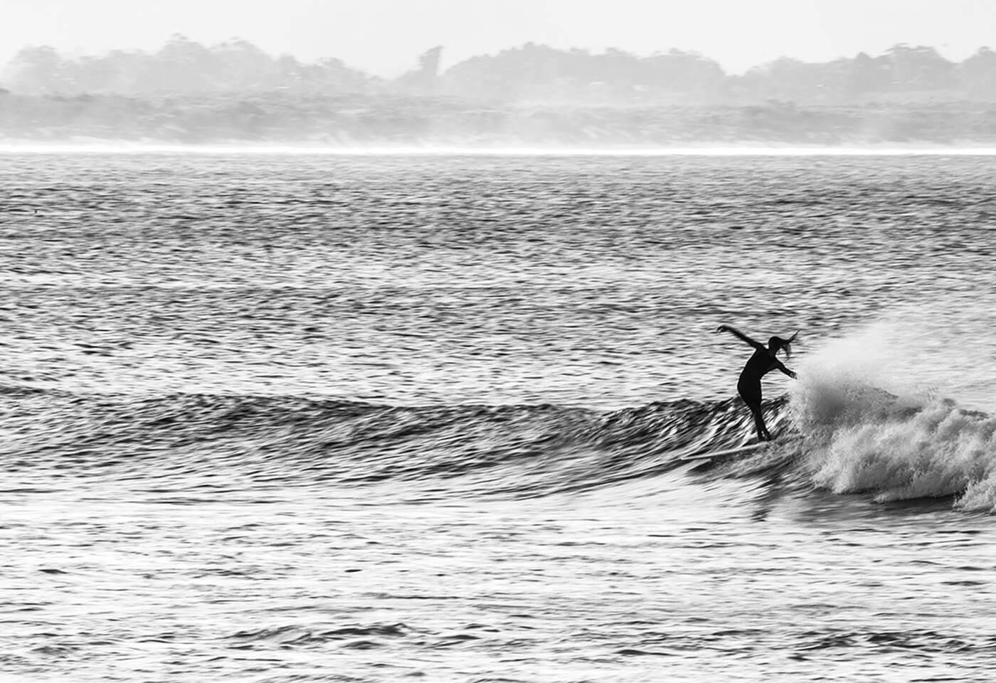 black and white image of a female surfer riding a wave